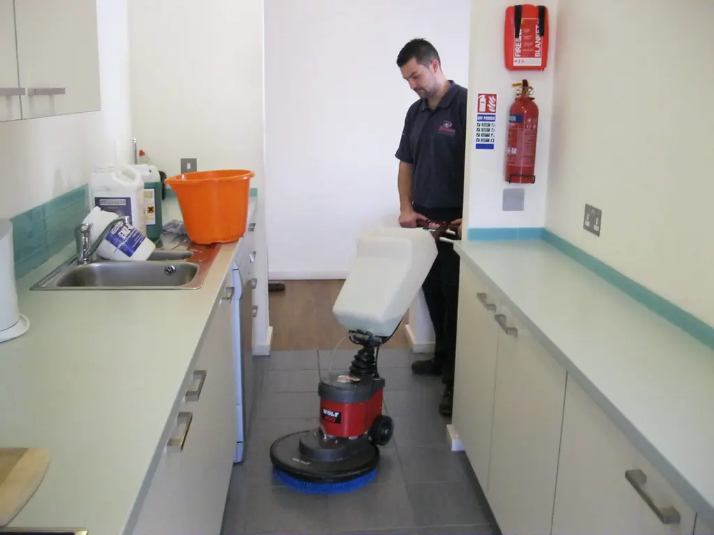 Técnico lavando o piso de uma copa com enceradeira